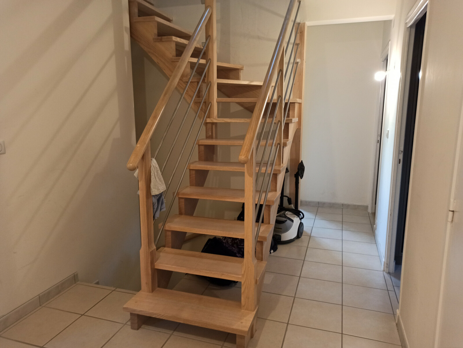 avant on voit un escalier en bois avec carrelage blanc terne et murs blancs